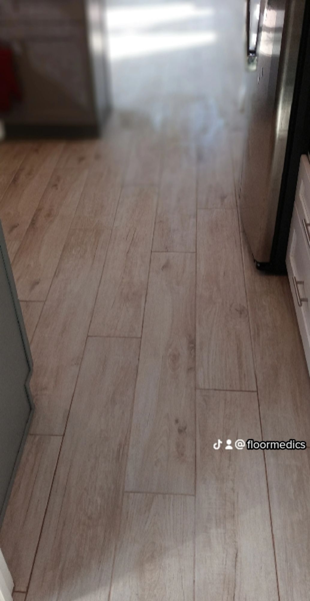 A kitchen with a wooden floor and a stainless steel refrigerator.