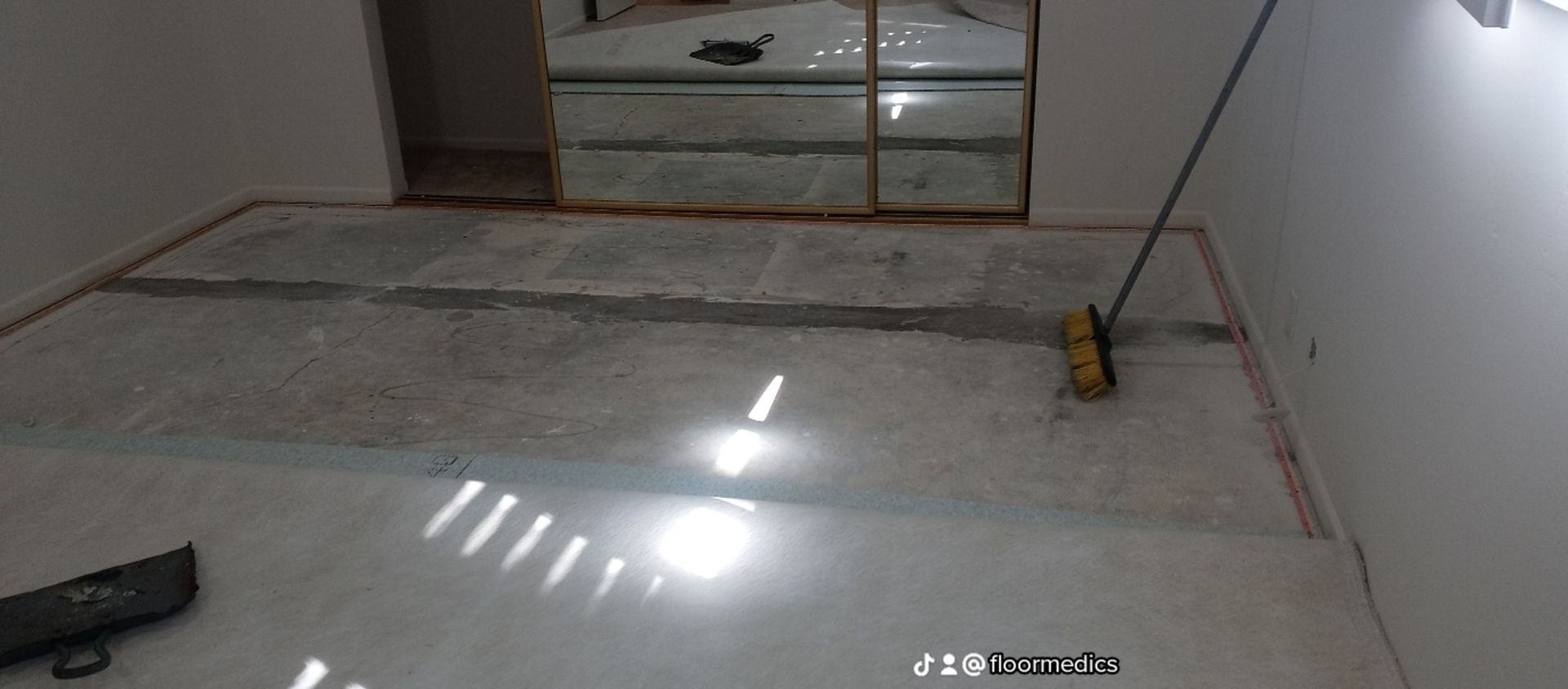 A room with a broom on the floor and a mirror on the wall.