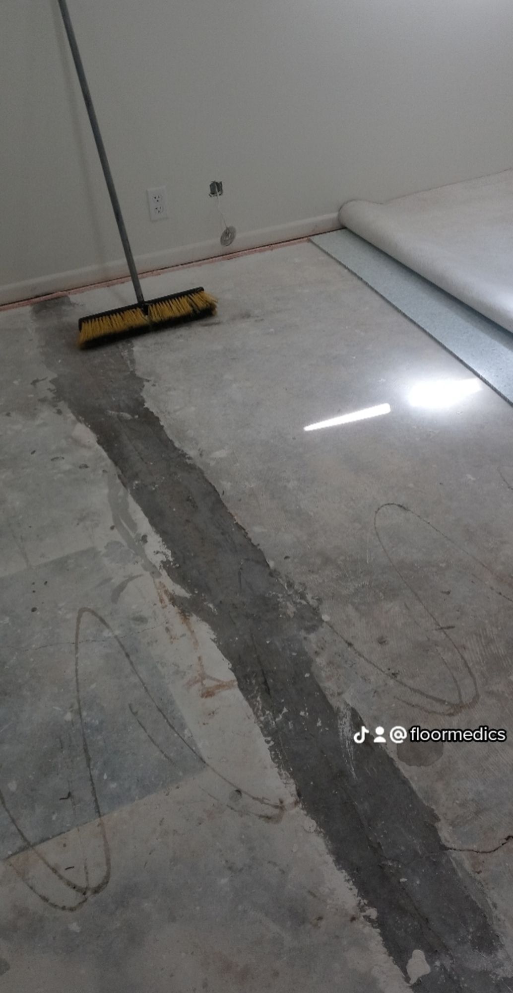 A broom is sitting on a concrete floor next to a wall.