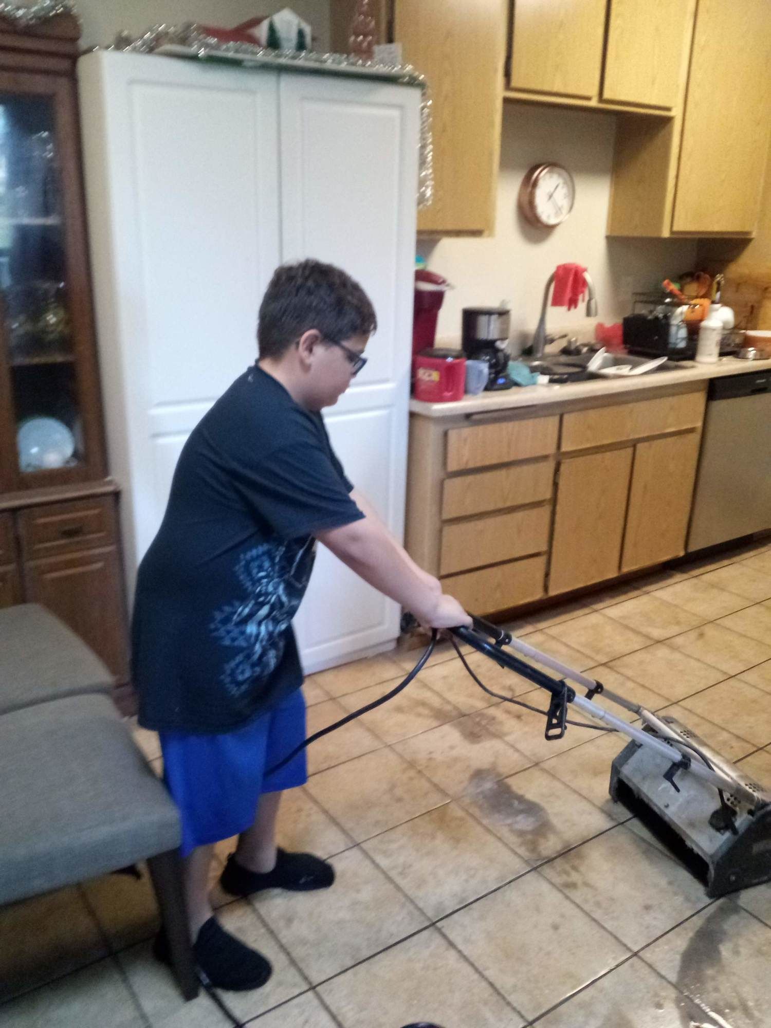 A young boy is using a vacuum cleaner in a kitchen