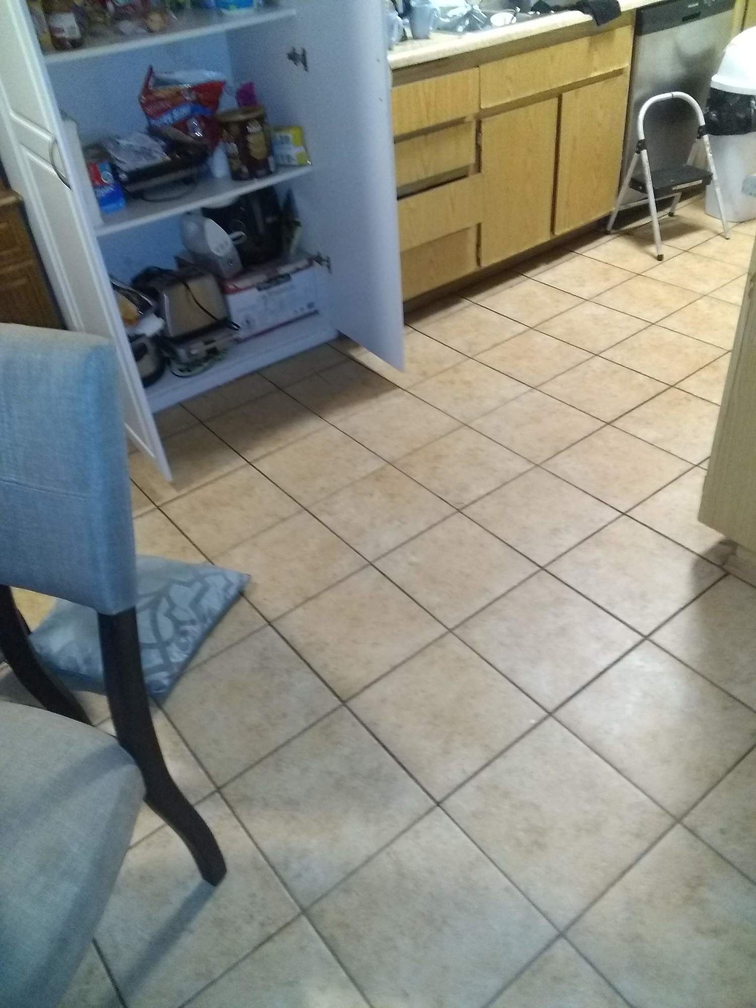 A kitchen with a tiled floor a chair and a cabinet