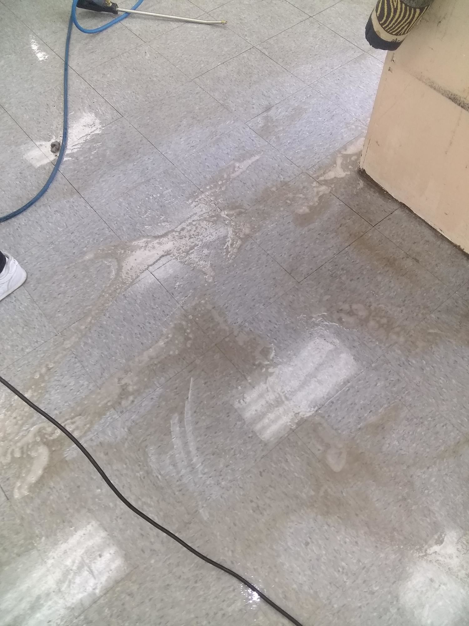 A person is cleaning a tiled floor with a vacuum cleaner.