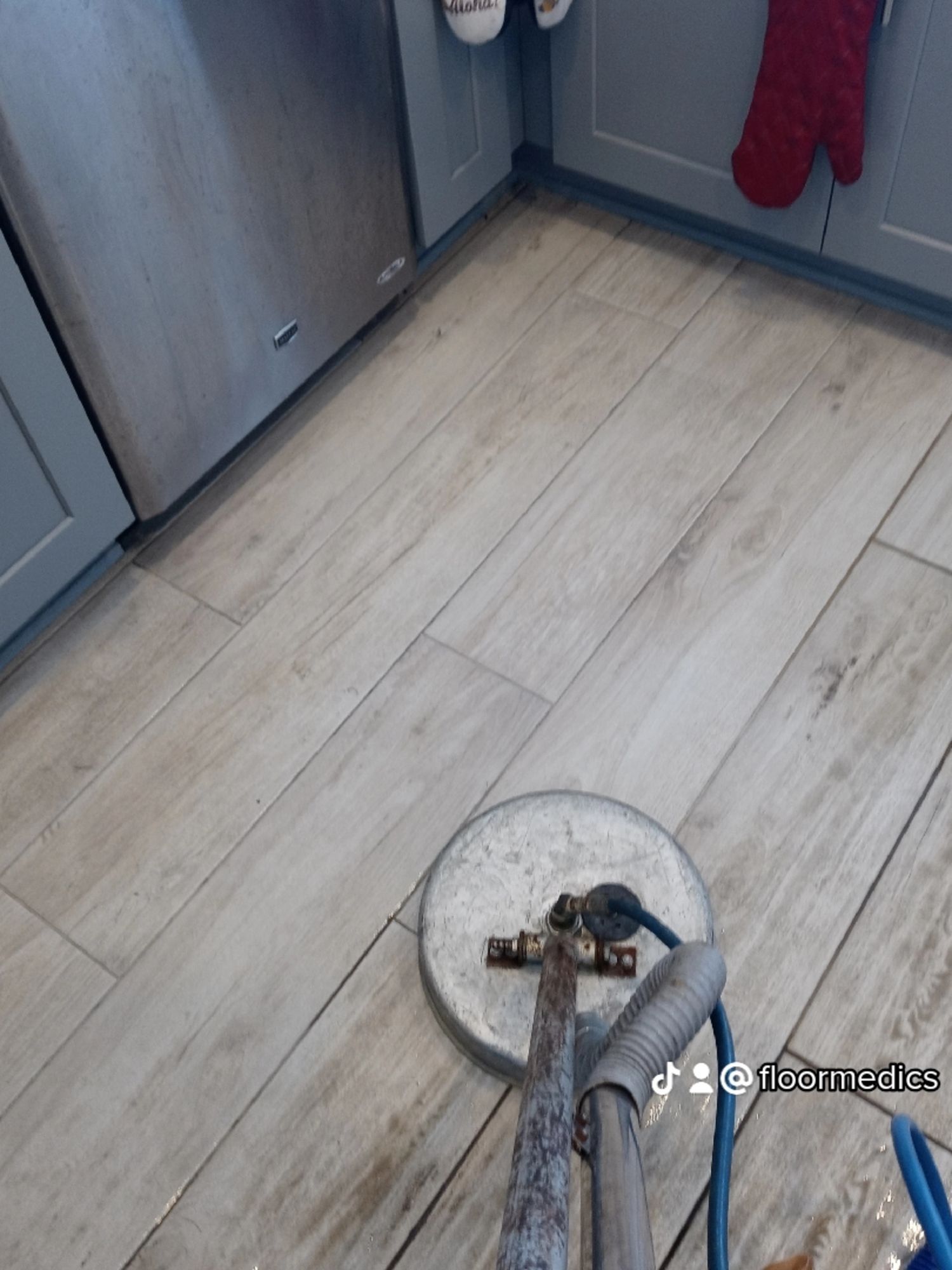 A vacuum cleaner is sitting on a wooden floor in a kitchen.