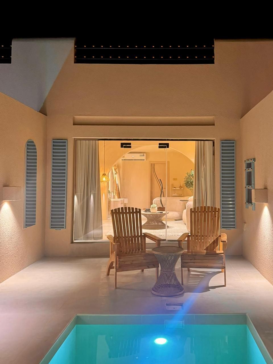 Outdoor patio with pool, leading to a warmly lit room with a seating area.