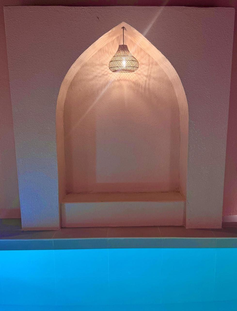 An alcove with a decorative lamp above a shelf, set against a pink wall, next to blue water.