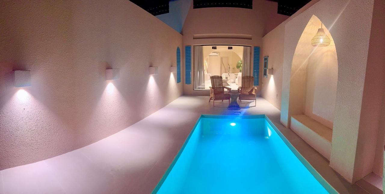 Poolside patio at night, illuminated, with a small pool, chairs and table, arched entry, and built-in bench.