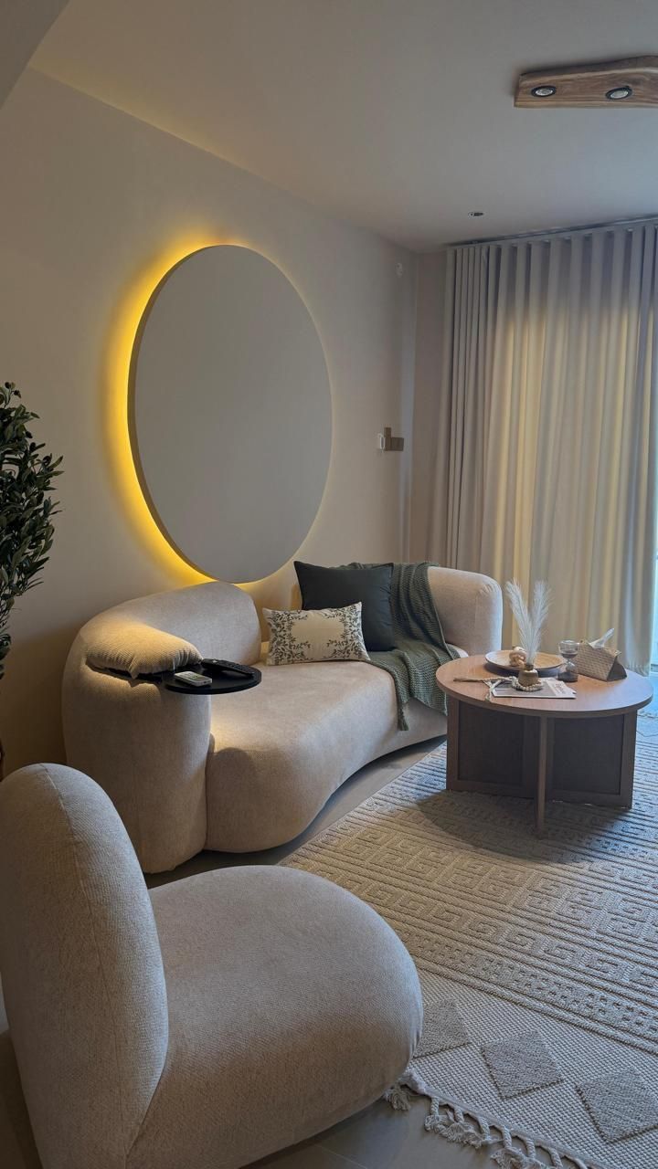 Cozy living room with curved cream-colored sofa, round coffee table, and large circular wall art with warm lighting.