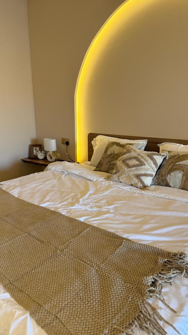 Bedroom with bed, neutral color scheme, illuminated semi-circle on wall above bed.