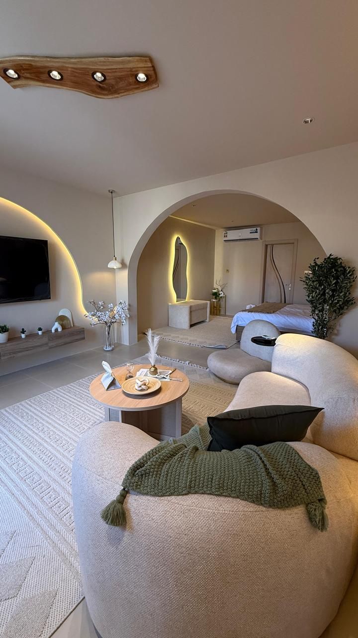 Cozy living room with curved walls, sofa, laptop, and view into a bedroom with a bed and vanity.