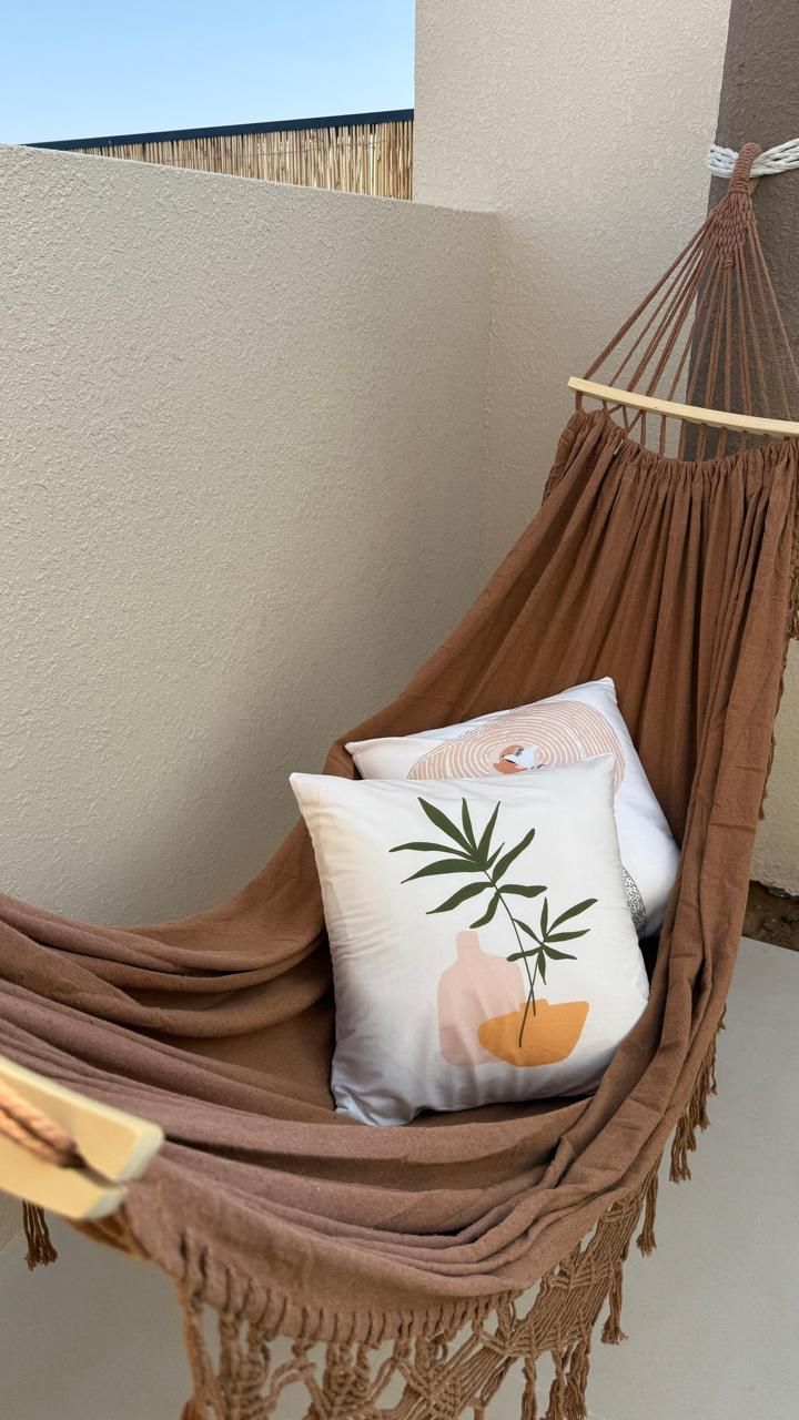 Brown hammock with pillows against a beige wall; outdoors.