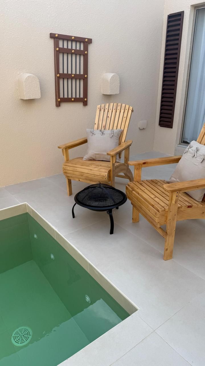 An outdoor seating area with a small pool. Two wooden chairs, fire pit, shutters, and wall decor.