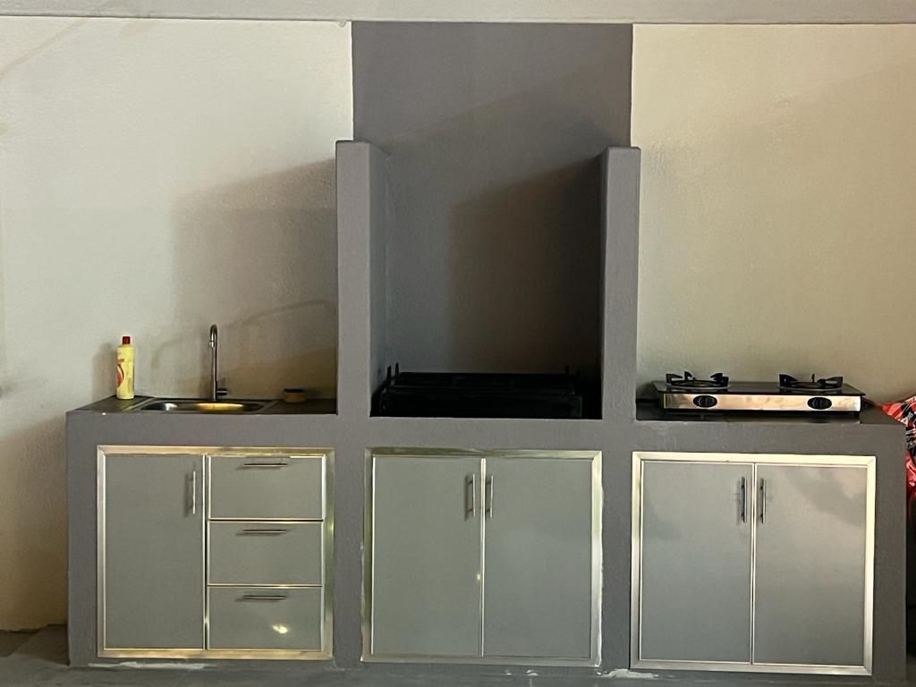 Outdoor kitchen with a grill, sink, cabinets, and a gas stove. Gray concrete with stainless steel accents.