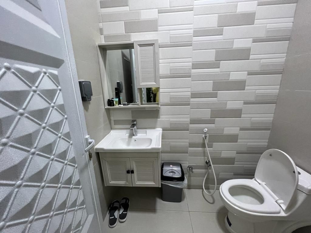 A small, modern bathroom with white and gray brick-style tile, a toilet, sink, and cabinet.