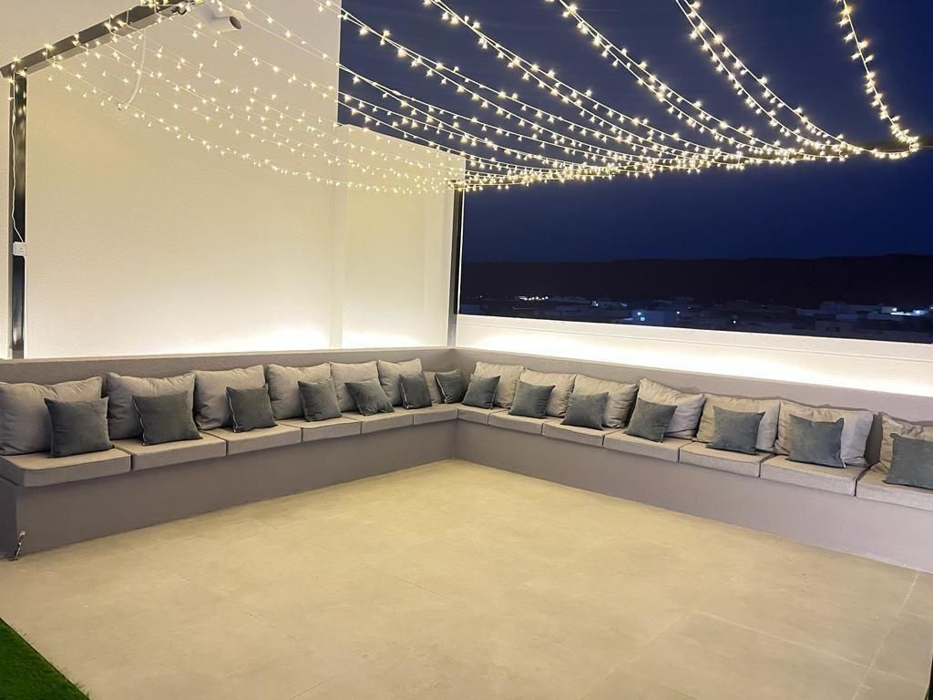 Outdoor seating area with grey cushions, string lights, and a view of the ocean at night.