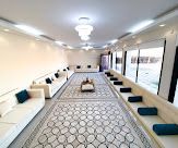 Spacious room with white sofas, large patterned rug, and windows.