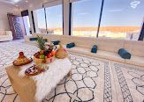 Living room with large windows overlooking a desert landscape. Low seating, decorative rug, and a coffee table with fruit.