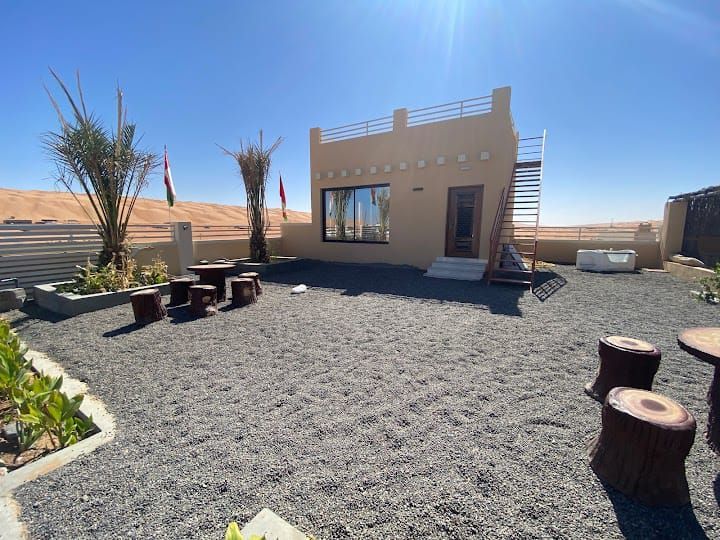Desert oasis house with outdoor seating, gravel yard, and stair access to the roof.