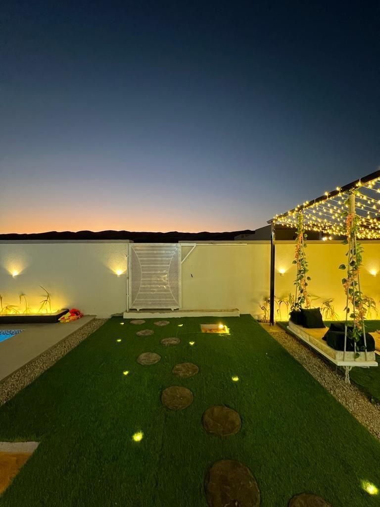 Backyard at dusk with a swing set, string lights, and a stone pathway leading to a gate.