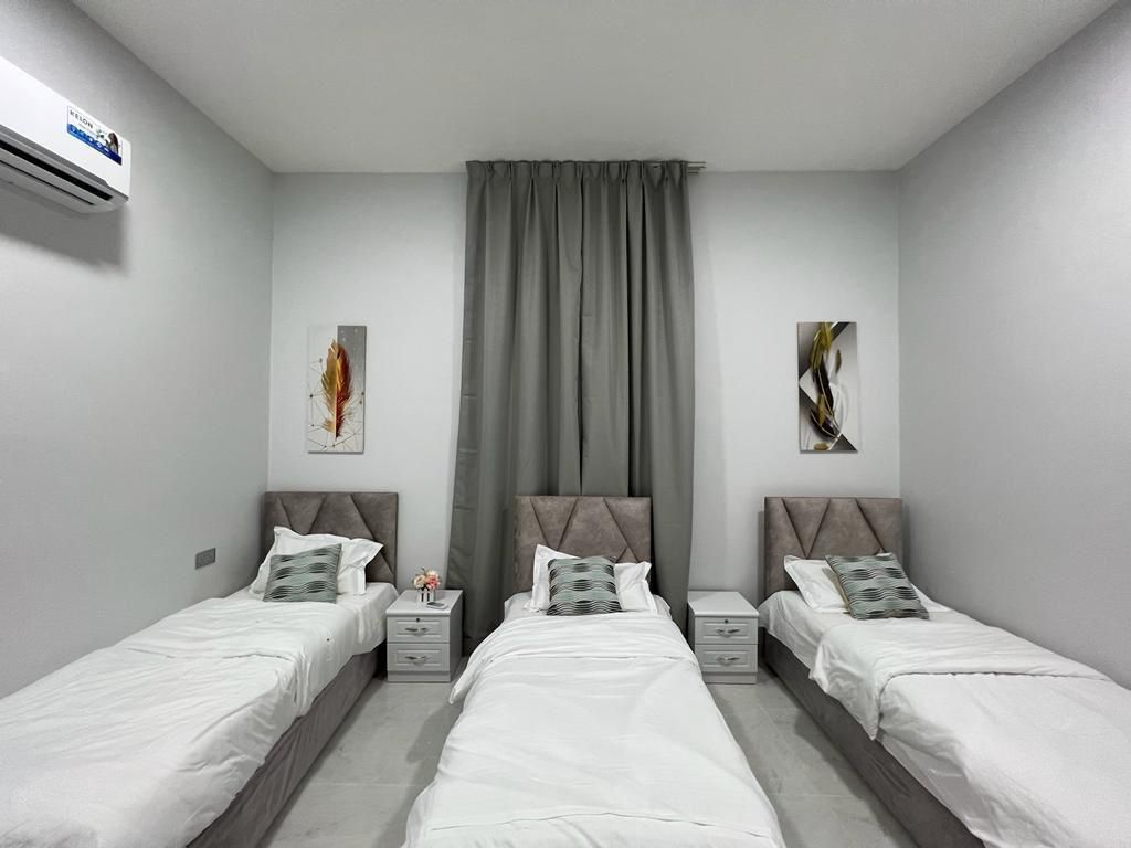 A bedroom with three twin beds, nightstands, and abstract art on the walls.