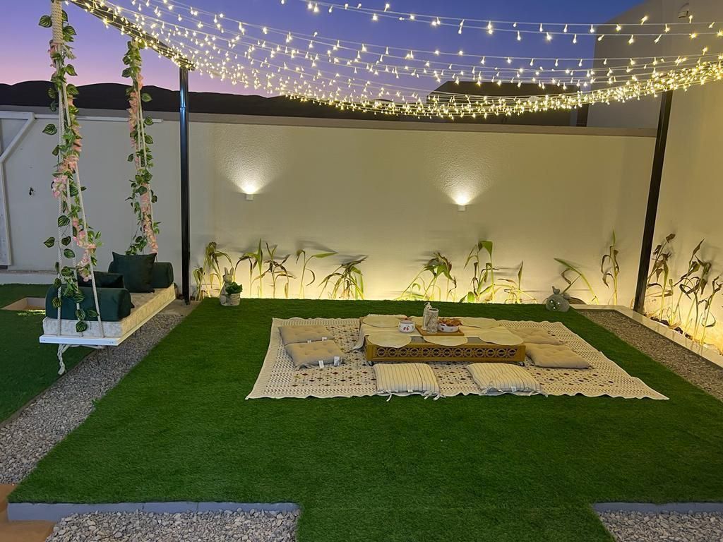 Outdoor patio with string lights, artificial grass, a seating area, and a swing, at dusk.