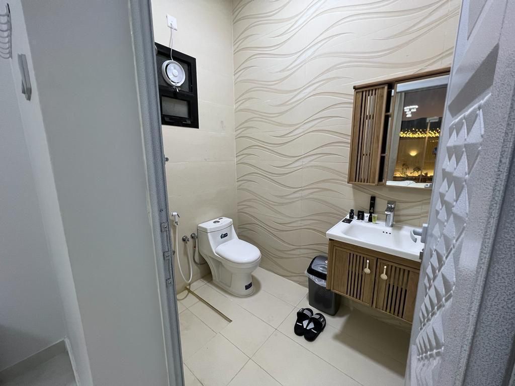 Bathroom with a toilet, sink, mirror, and wavy patterned wallpaper.