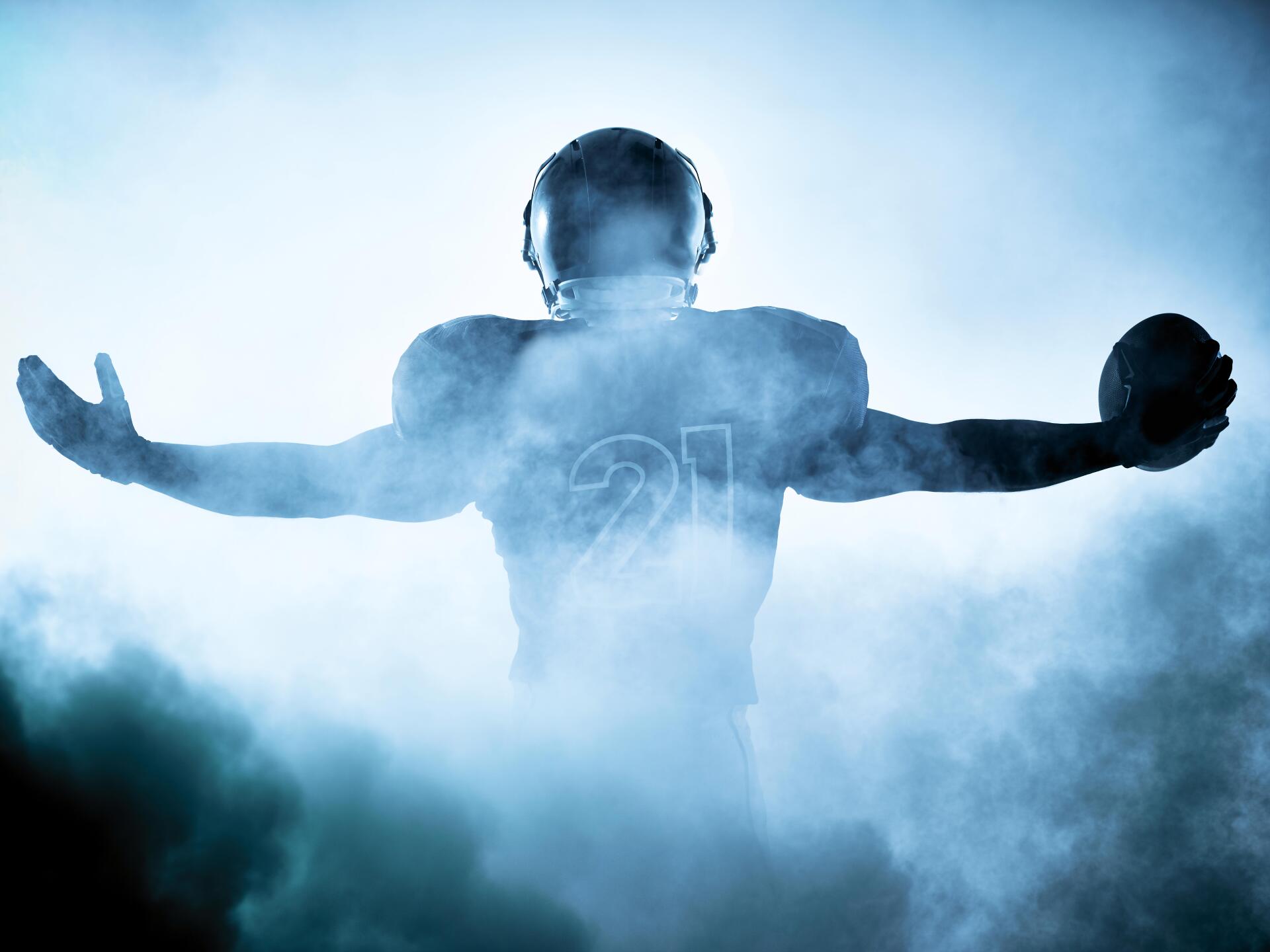 A football player is standing in a cloud of smoke with his arms outstretched.