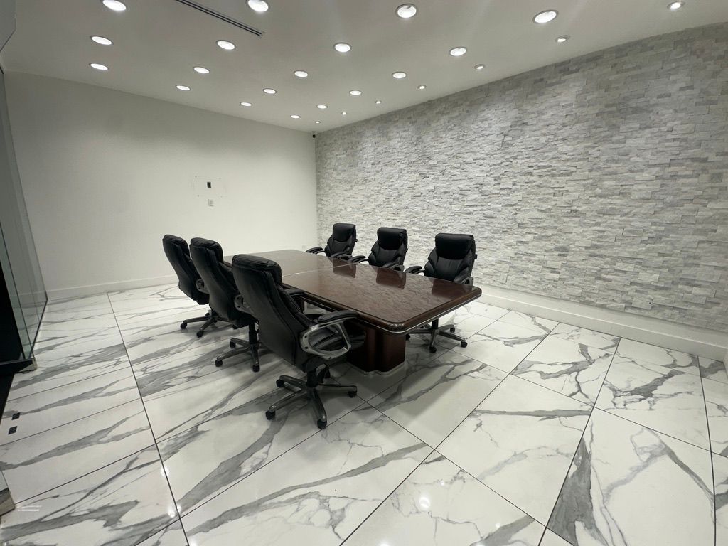 Conference room with long wooden table, black chairs, marble tile floor, and stone accent wall.