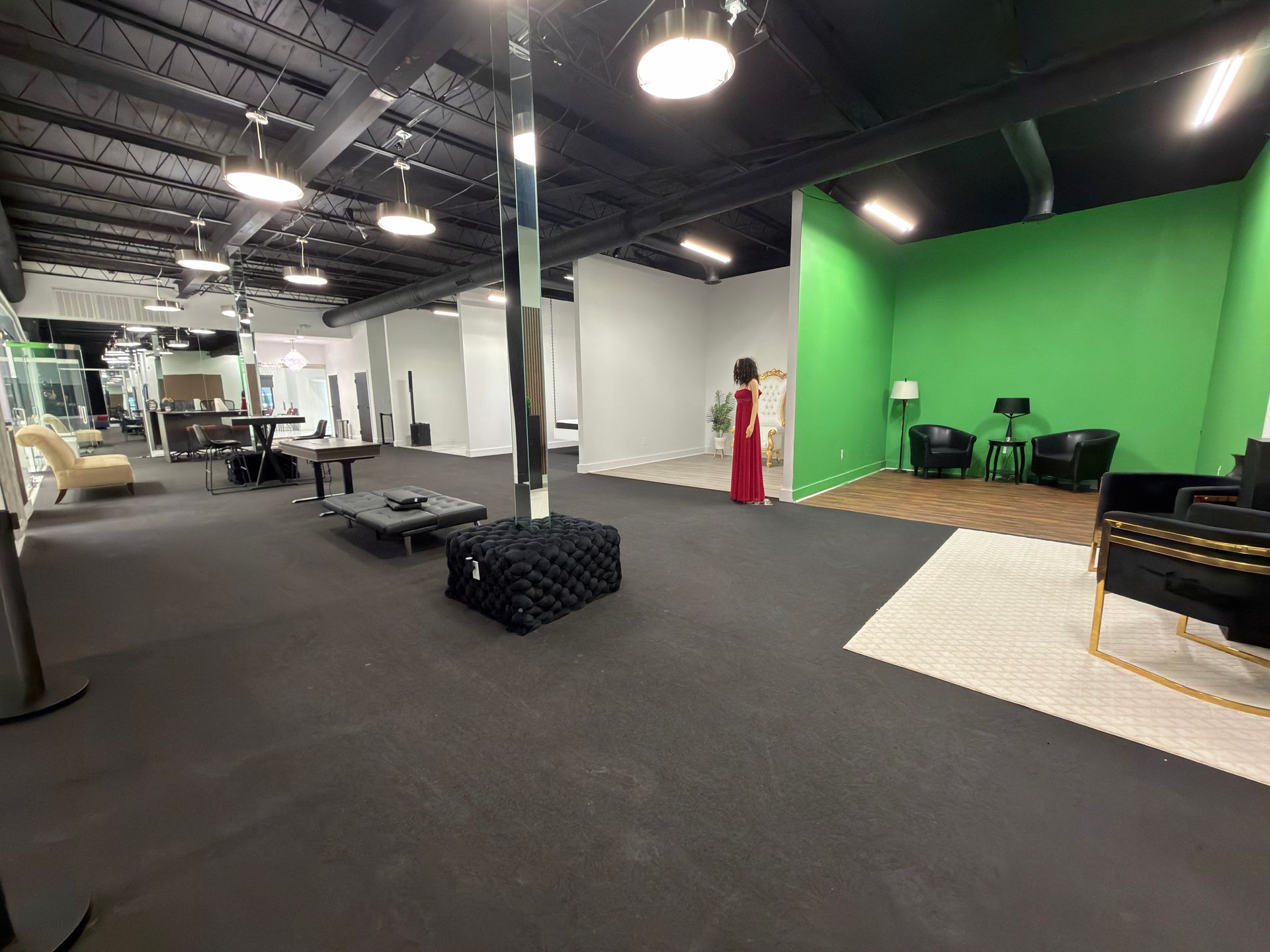 Open-concept studio with a green screen, furniture, and a person in a red dress. Black floor and ceiling.