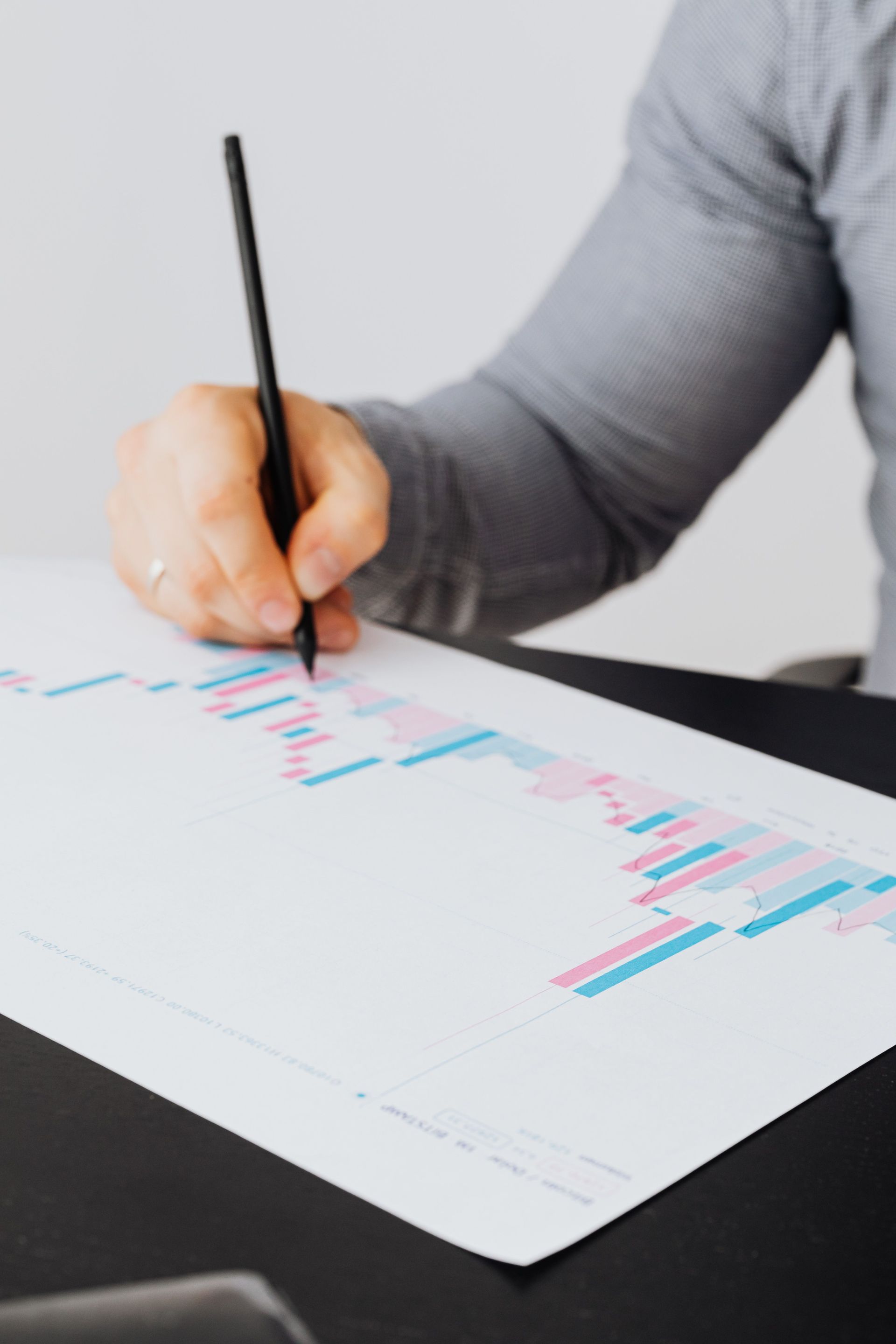 Hand holding a pen over a chart with pink and blue bars on a desk