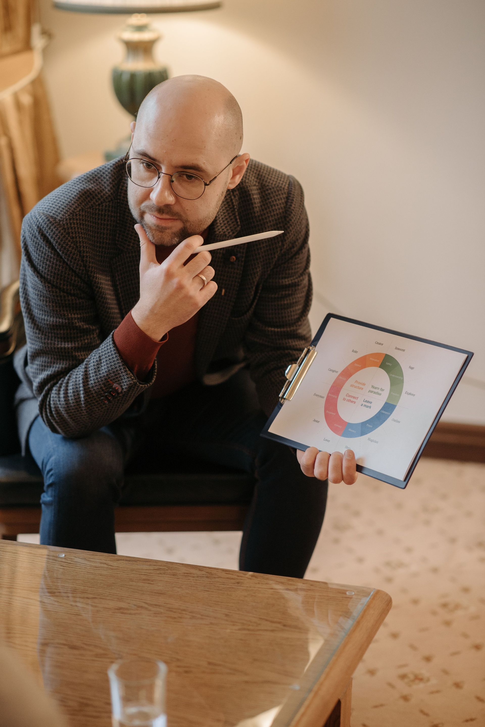 Man holding a clipboard with a colorful circular chart, seated indoors and looking thoughtfully at the camera.