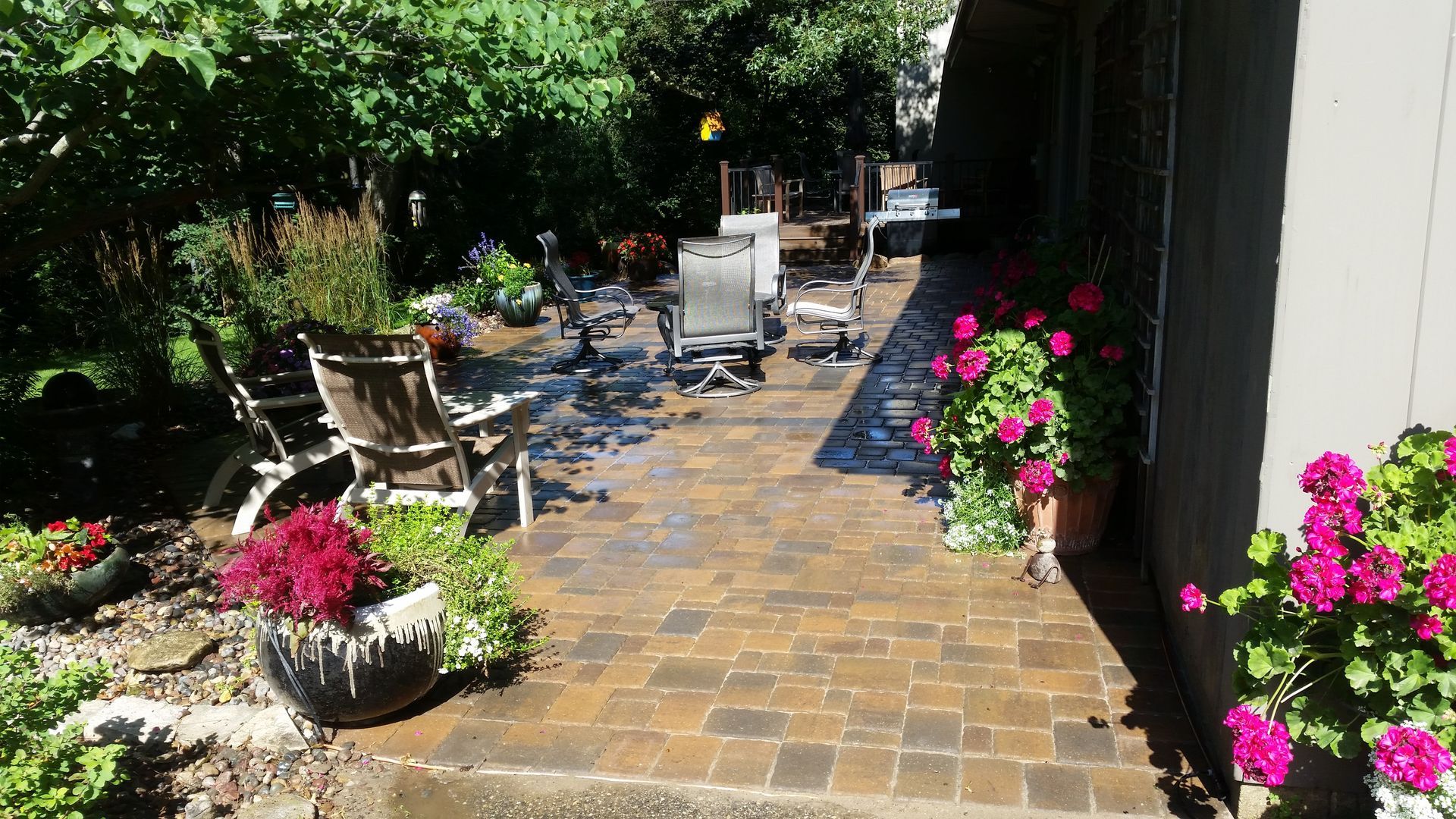 A paved stone patio with outdoor furniture, potted plants, and vibrant pink flowers next to a building.