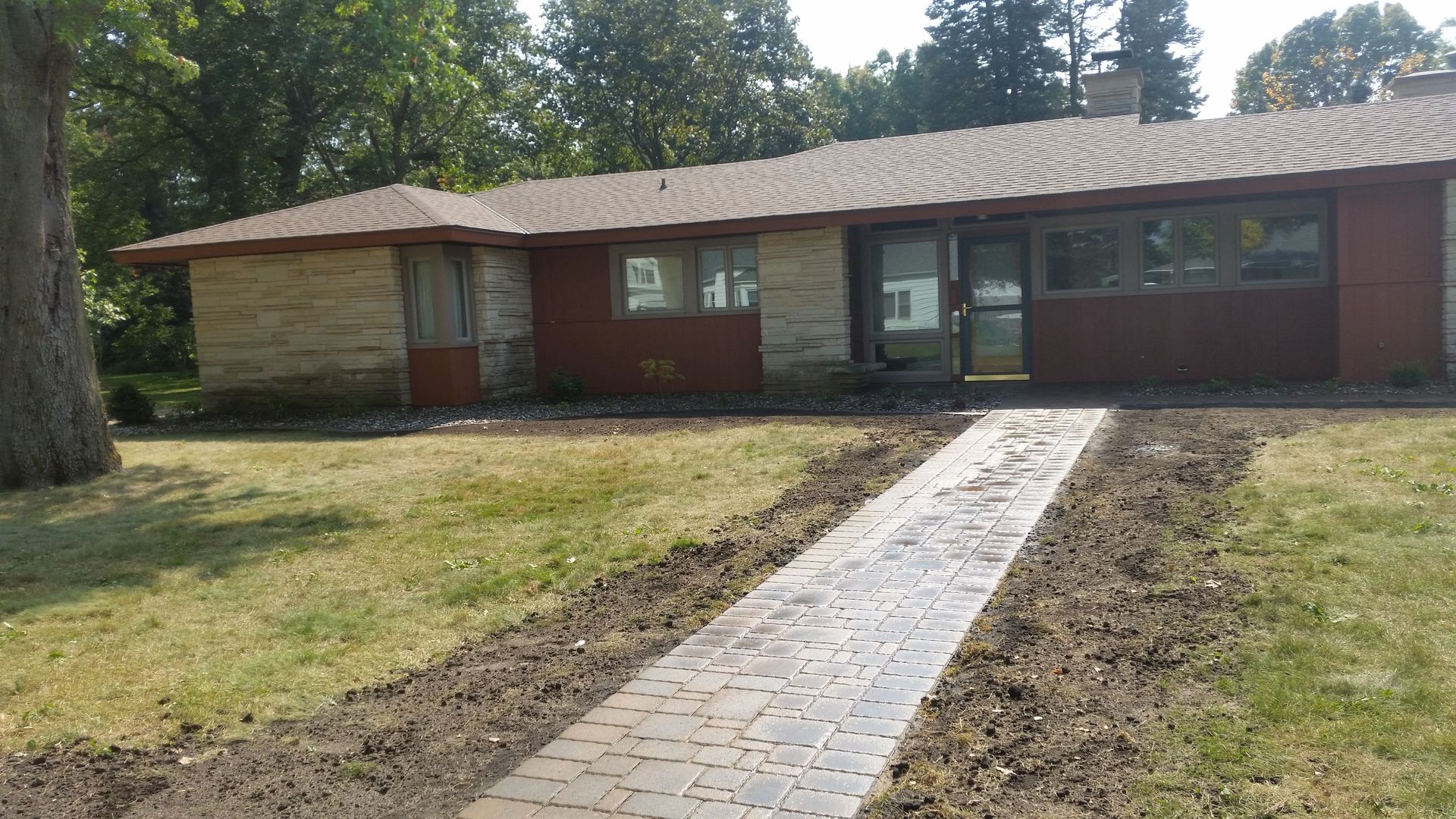 A single-story brick and stone house with a newly installed paved walkway leading to the front entrance.