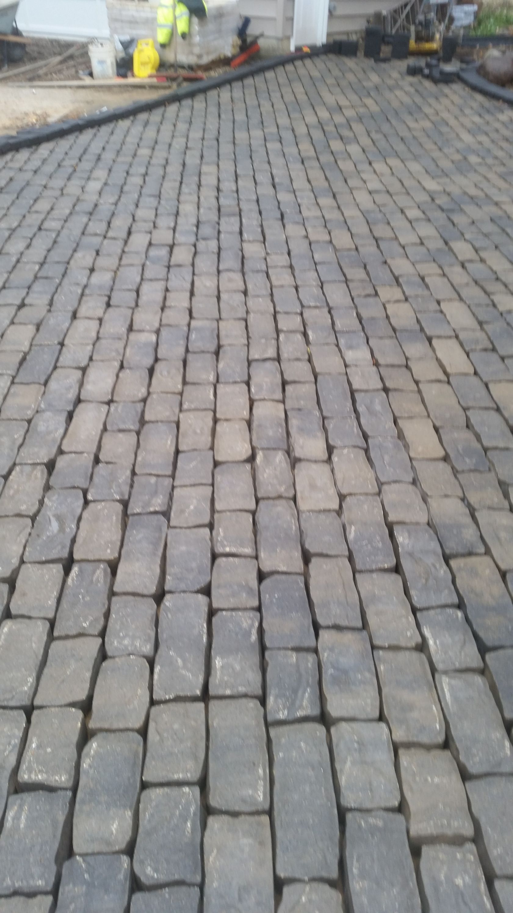 A close-up of a recently installed grey cobblestone driveway surface with workers in the background.