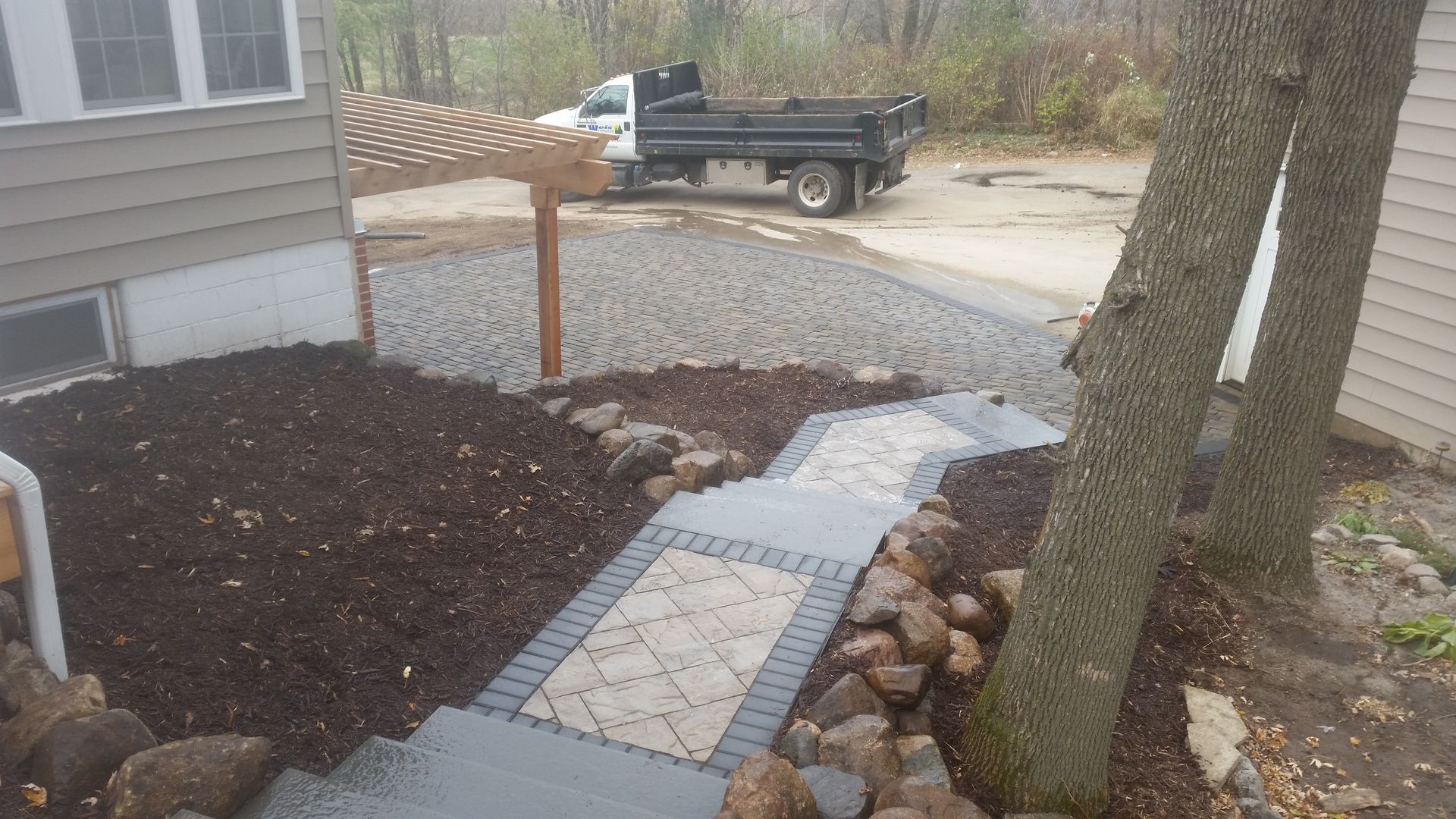 A new stone path and patio area under construction next to a house, with fresh mulch, landscaping, and a dump truck.