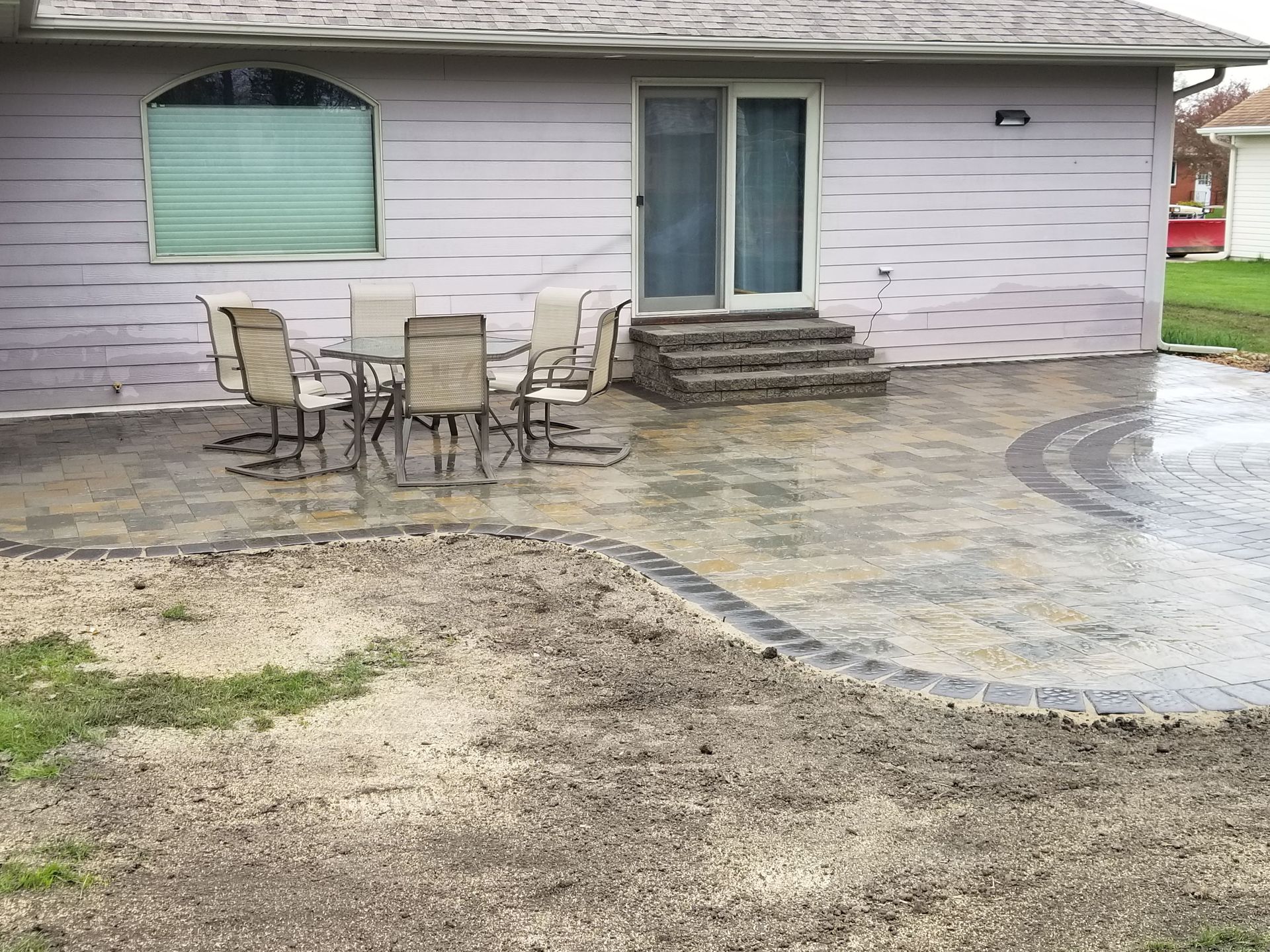 A stone patio with a table and chairs outside a light pink house with a sliding glass door and stone steps.
