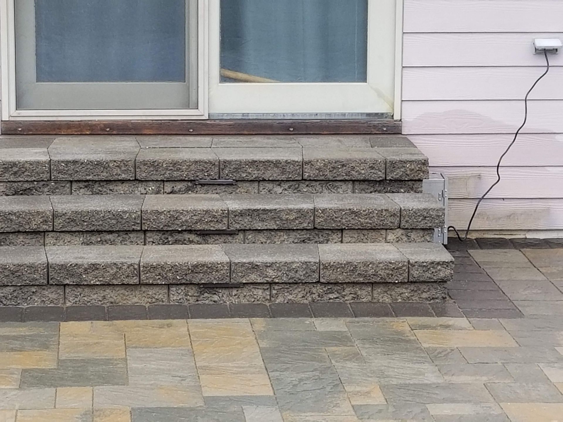Three gray stone steps leading up to a sliding glass door above a multi-colored stone patio.