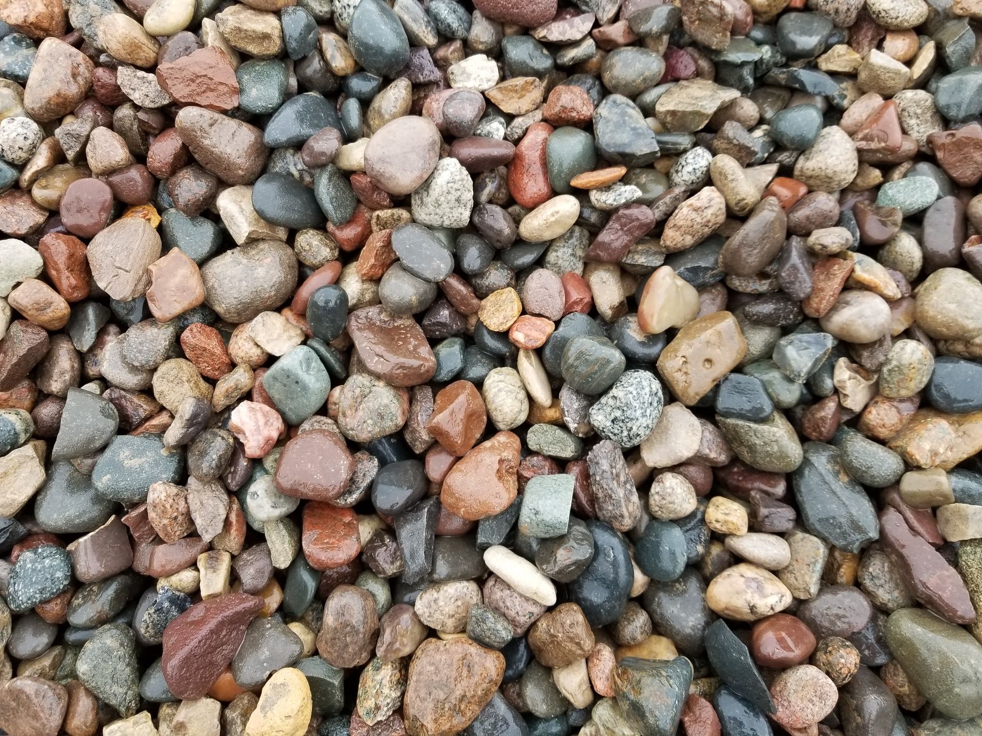 A close-up view of a pile of smooth, multicolored river stones and pebbles in various earthy shades.