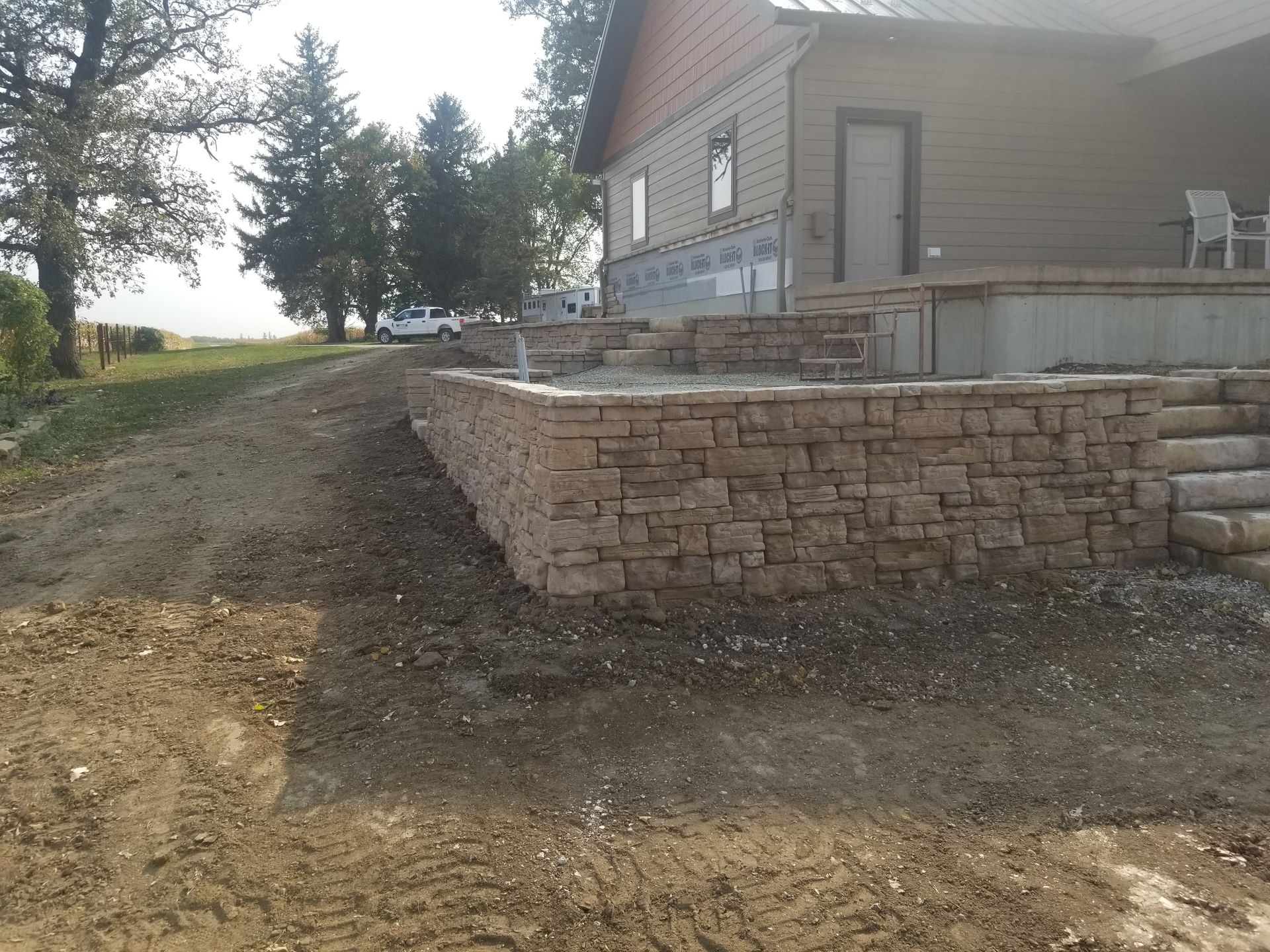 A new stone retaining wall stands in front of a house, leading toward a set of steps under construction.