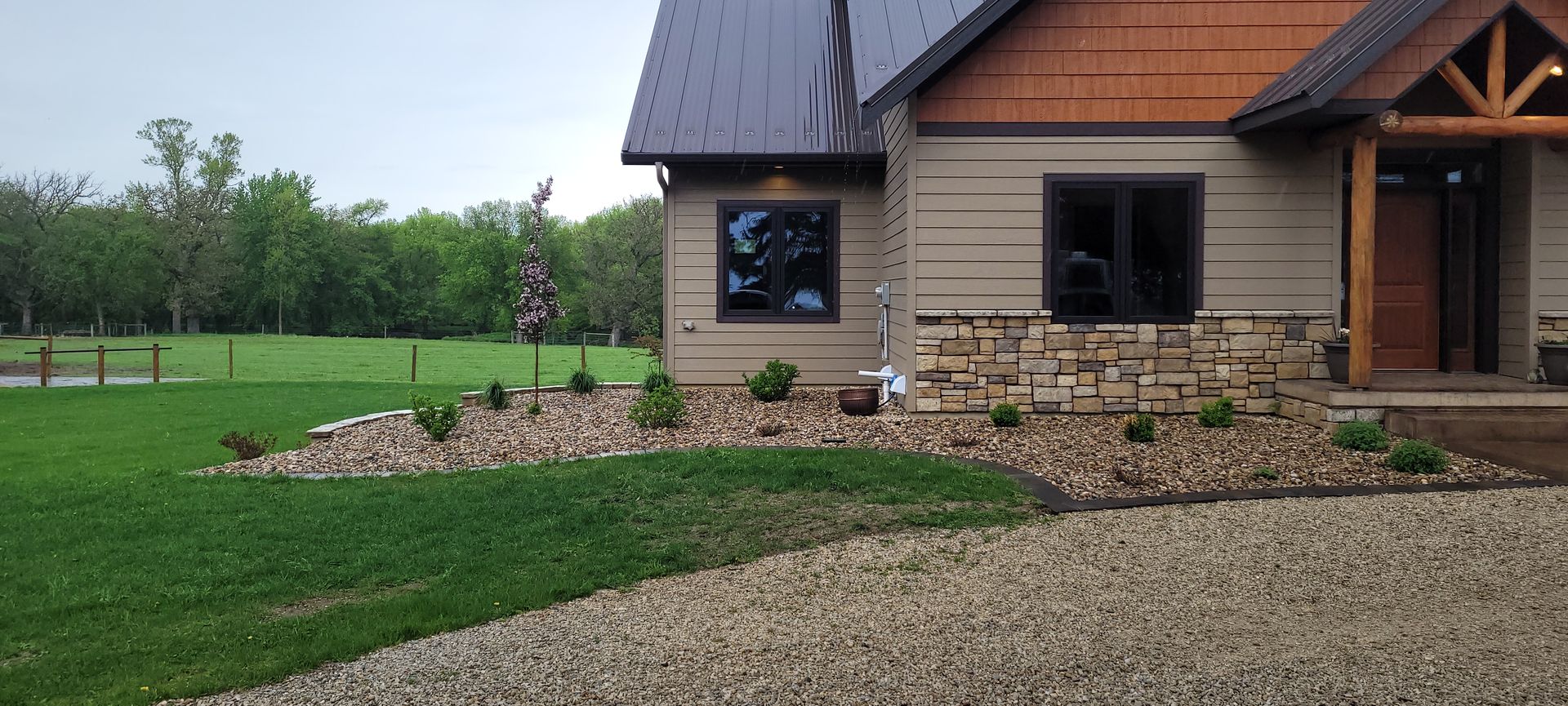 A modern home with tan siding and stone masonry, featuring a landscaped gravel garden in front of a green lawn.