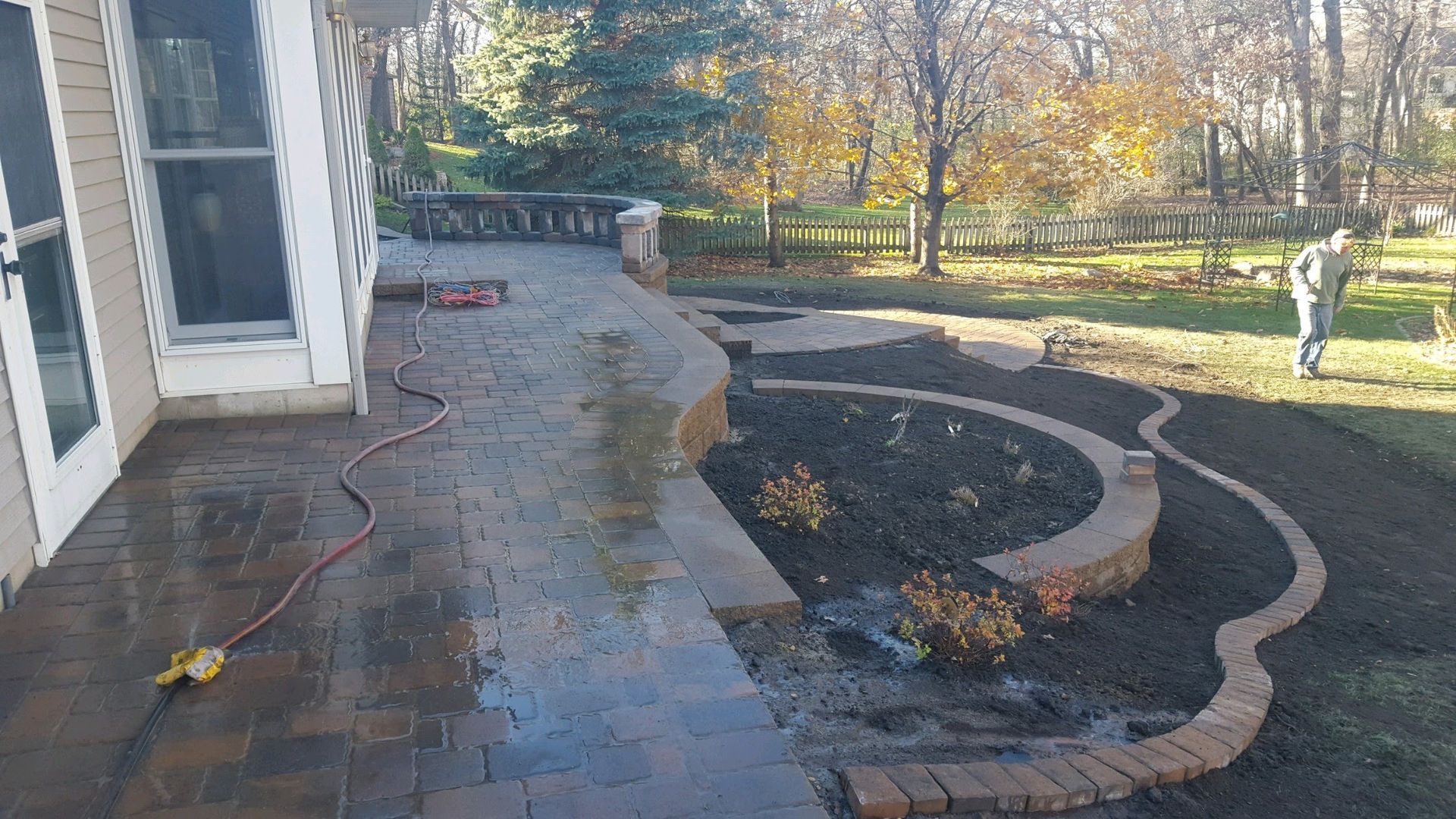 A newly paved stone patio with curved brick retaining walls and garden beds, adjacent to a house with a screened door.