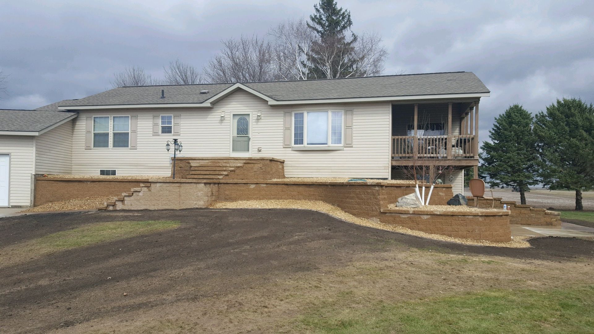 A light-colored house featuring a new stone retaining wall and terrace steps leading up to the front entrance.