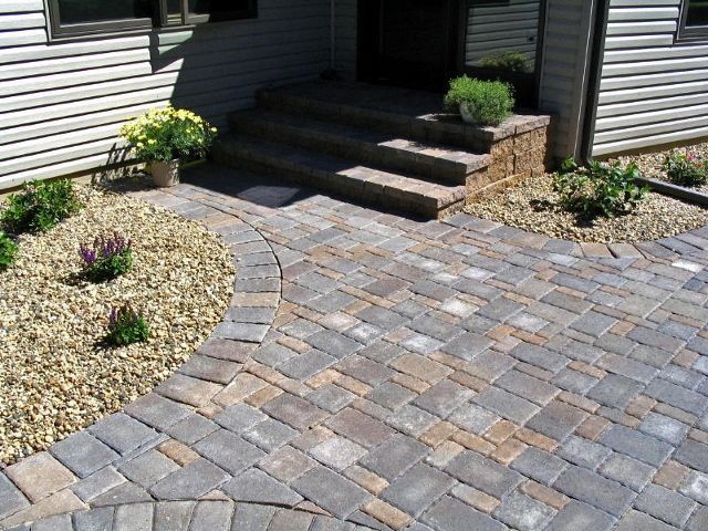 A paver walkway leads to a front door with stone steps, surrounded by landscaping beds with gravel and small shrubs.