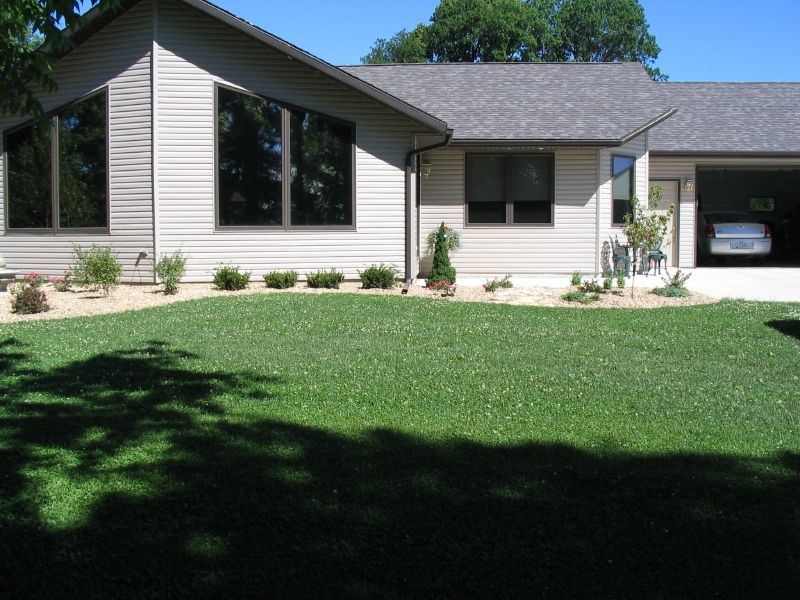 A beige house with large, angled windows, a garage, and a manicured lawn under a clear blue sky.
