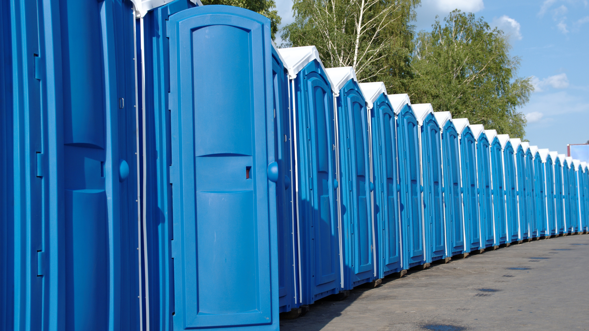 Row of blue portable toilets lined up outdoors.