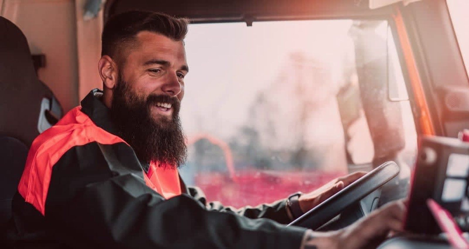Smiling driver in an orange safety vest, looking at phone while driving a vehicle.