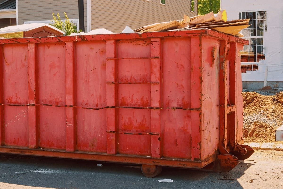 Red construction dumpster filled with debris on a street.