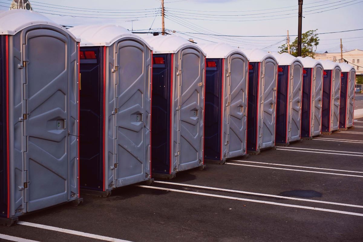 A row of portable toilets on asphalt, gray doors, red trim.