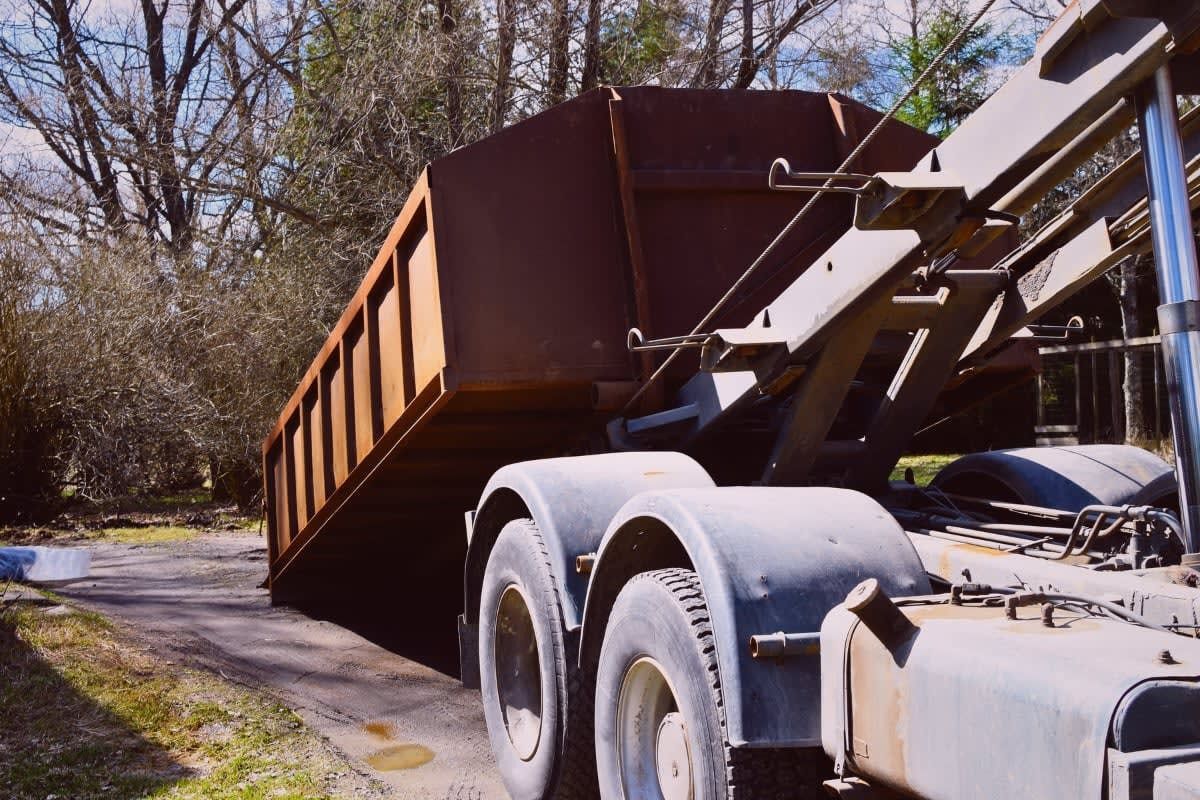 Brown dumpster being lifted by a truck in a residential area.