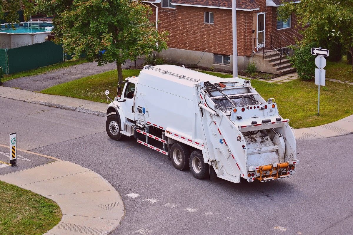 White garbage truck driving on a residential street.