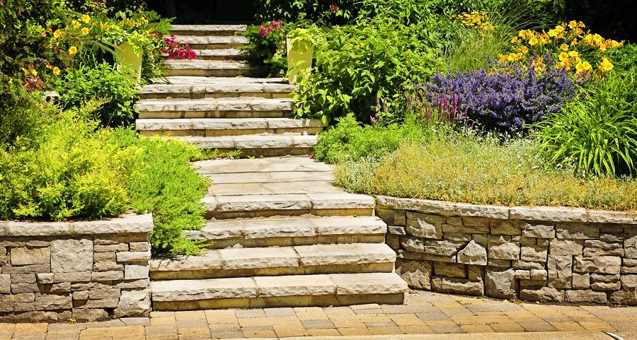 natural stone steps leading down to a paver patio with gardens on both sides of the steps 